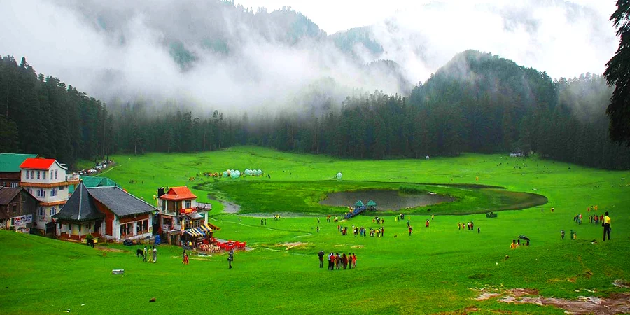 Lush green Khajjiar meadows surrounded by tall pine trees with families relaxing.